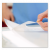 Mitarbeiter zeigt die selbstklebende, transparente Folie, die beidseitig auf das Druckprodukt aufgebracht worden ist.